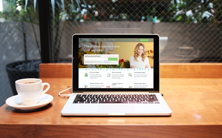 A laptop with Create's website loaded on it, resting on a coffee bench with coffee beside