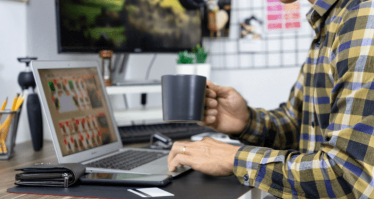 A person browsing their laptop in their home office holding a mug