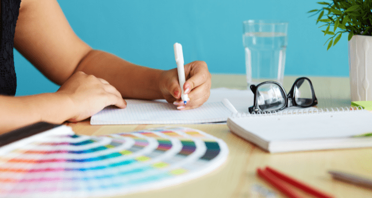 A person writing at a desk with a colour wheel to one side