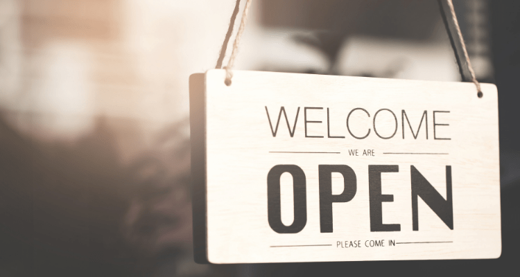 Welcome, we are open sign hanging on a glass door in dawn light