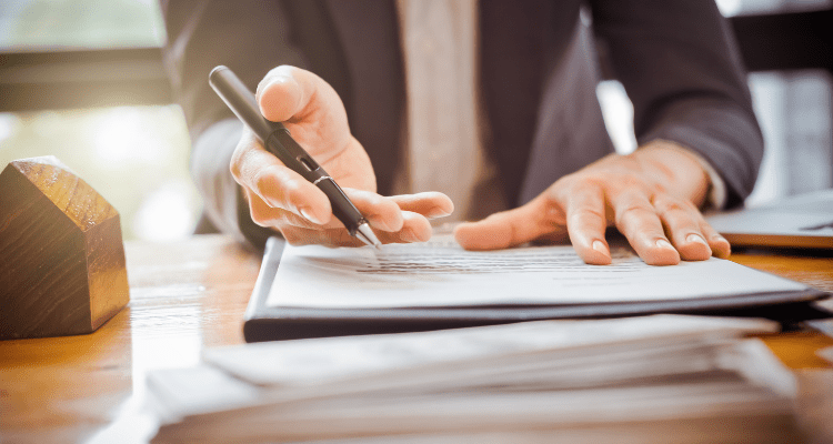 A person in a suit with an outstretched hand holding a pen working on documents