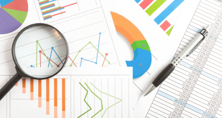 A pile of statistical charts spread on a table with a pen and magnifying glass laying on top