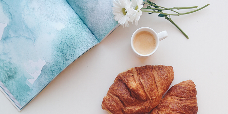 Stock image from Foodies Feed of a croissant, tea, flower and book 
