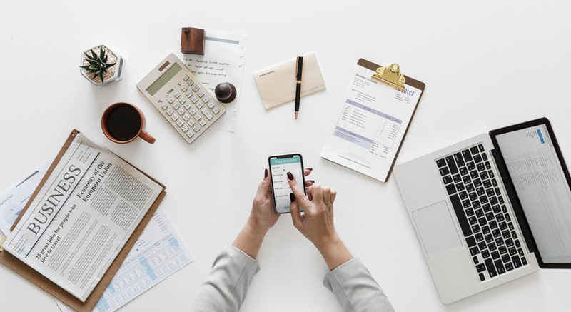 An assortment of office stationery and paperwork with a person scrolling their phone central