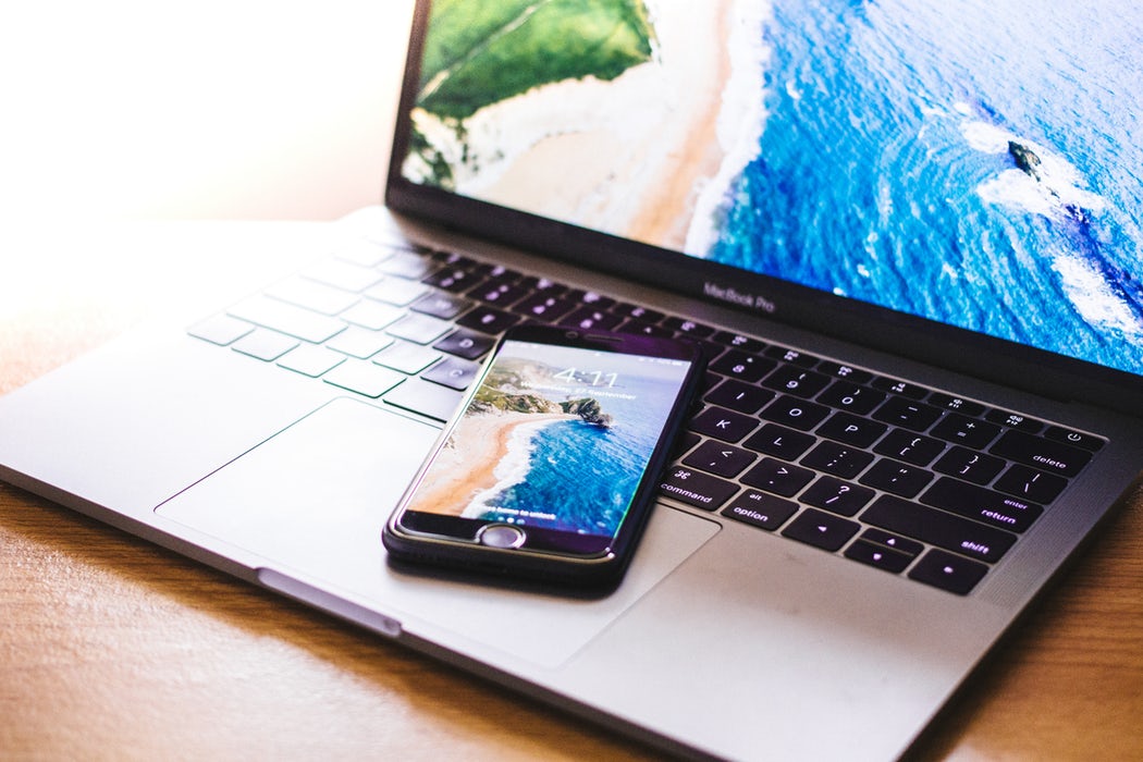 A mobile phone resting on a laptop, both with a vibrant beach background