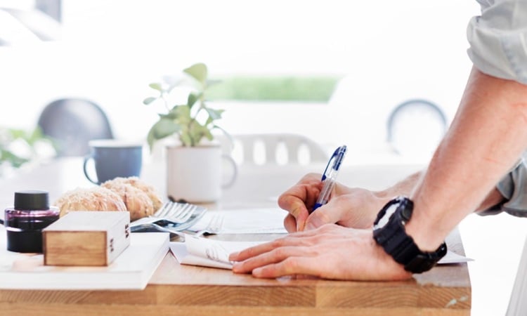 Person writing at a wooden desk