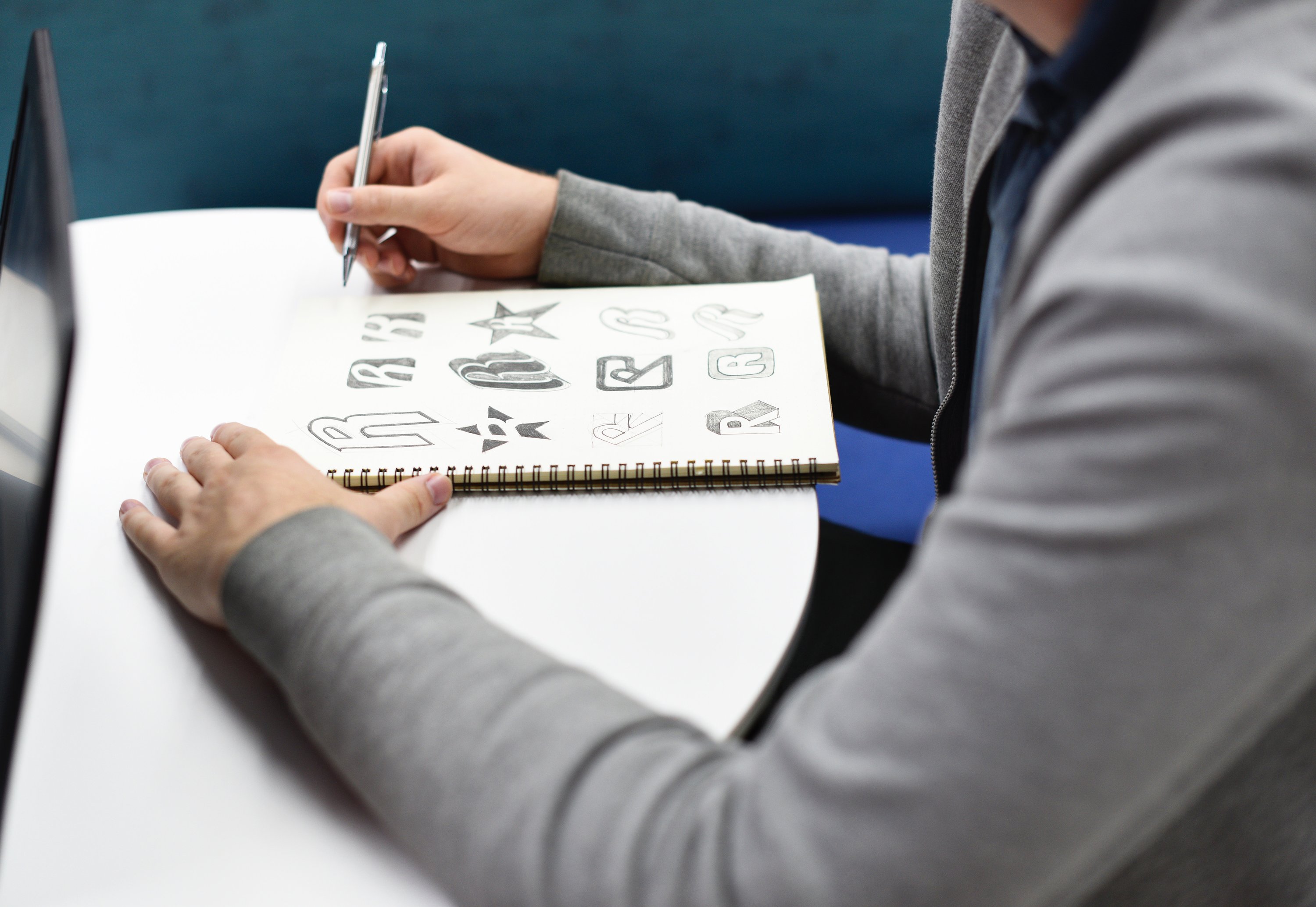 A person sitting at their desk working on drawing several logo variations in their sketchbook