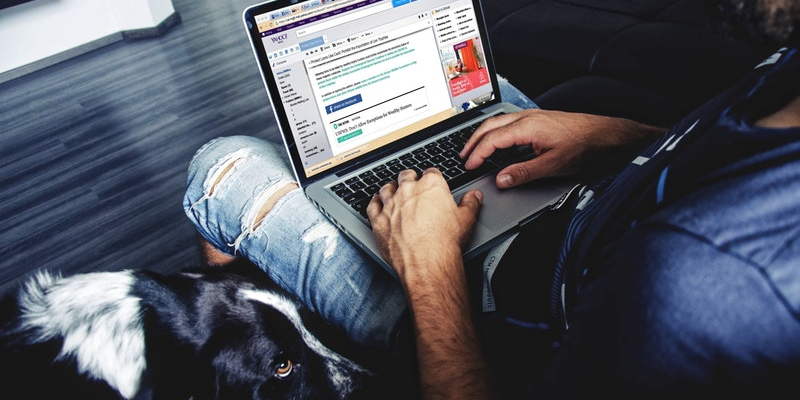 A person with their computer on their lap browsing emails with their dog at their side