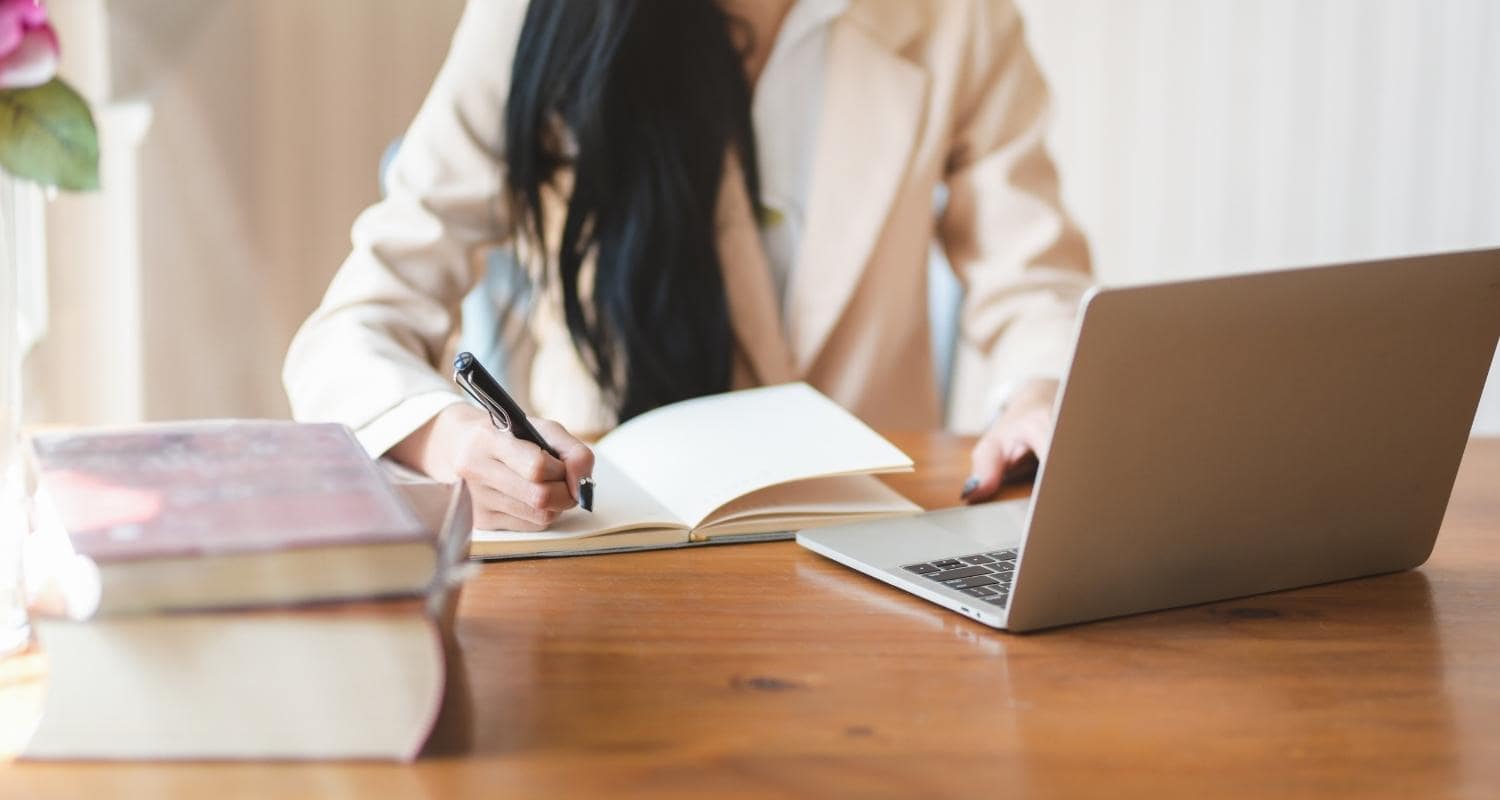 A person writing in a notepad at their desk