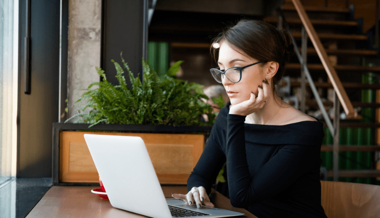 A person wearing glasses sitting at a table working on their laptop