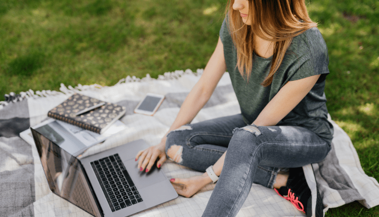 A person sitting on a blanket outside on the grass working on their laptop