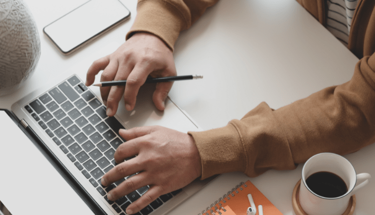 A person working at their laptop with pen in hand